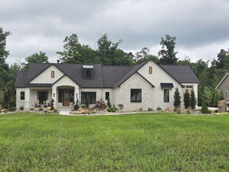 white board and batten home with stone accents and a dark shingle roof