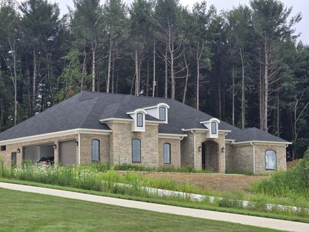 brick and stone ranch home with a dark shingle roof and arched windows