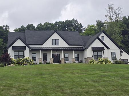 white farmhouse exterior with a black shingle roof and standing seam metal awnings