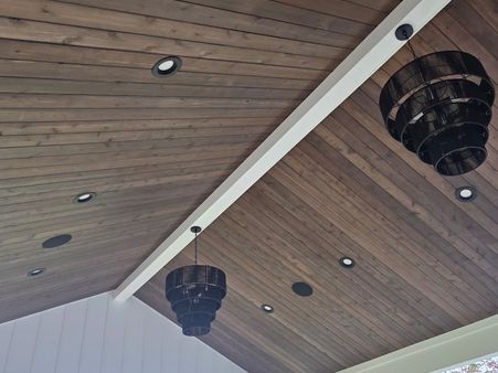 covered porch with a stained wood plank ceiling and black chandeliers