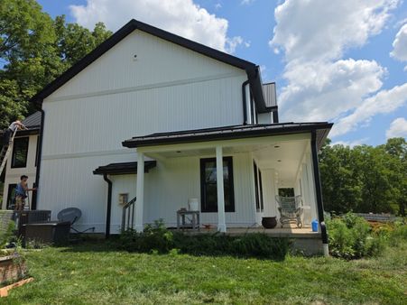 white board and batten farmhouse with a black standing seam metal roof and covered porch