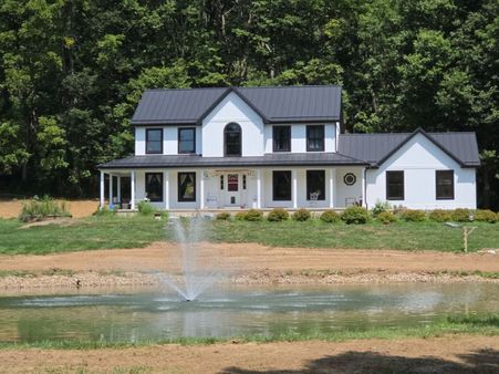 white farmhouse with a black metal roof and arched window overlooking a pond